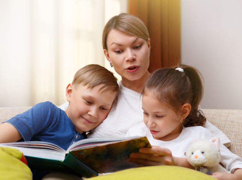 Mama czytająca książkę przytulonym do siebie synowi i córce na kanapie